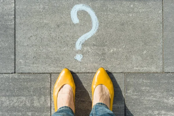 Woman feet with question mark in front of her legs painted on the asphalt