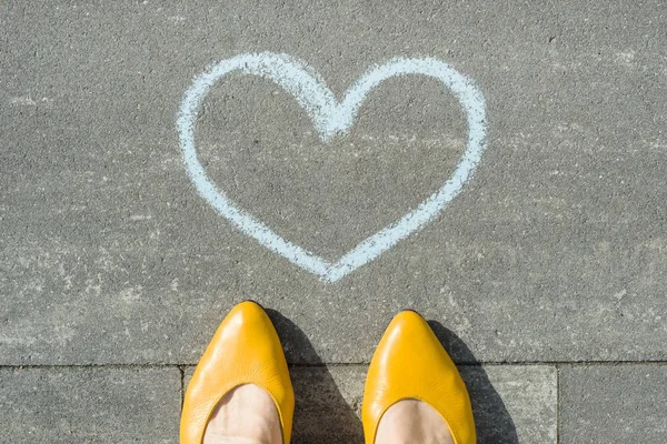 Pés femininos com símbolo do coração azul pintado no asfalto . — Fotografia de Stock