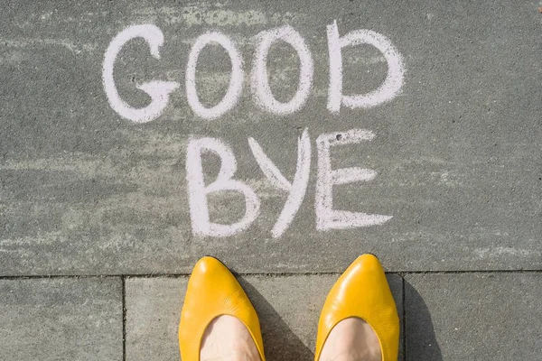 Female feet with text goodbye written on grey sidewalk