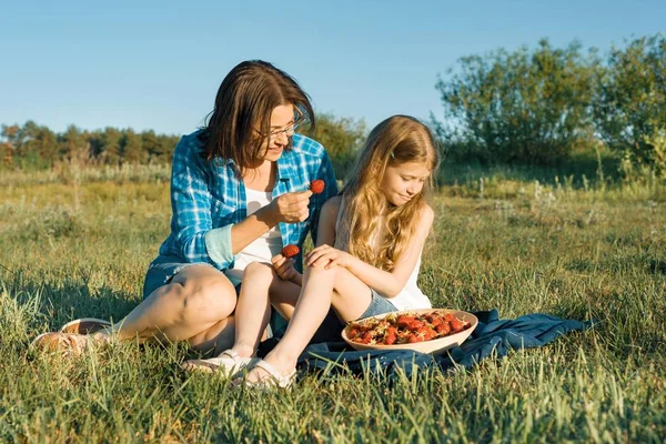 Mama i córka w przyrodzie, kraju wakacji, matka i dziecko siedząc na trawie, jeść truskawki — Zdjęcie stockowe