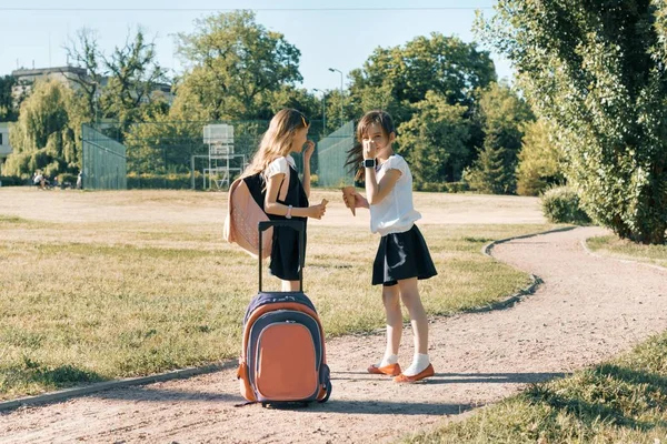 Вид ззаду на двох дівчат-школярок з рюкзаками, що їдять морозиво — стокове фото