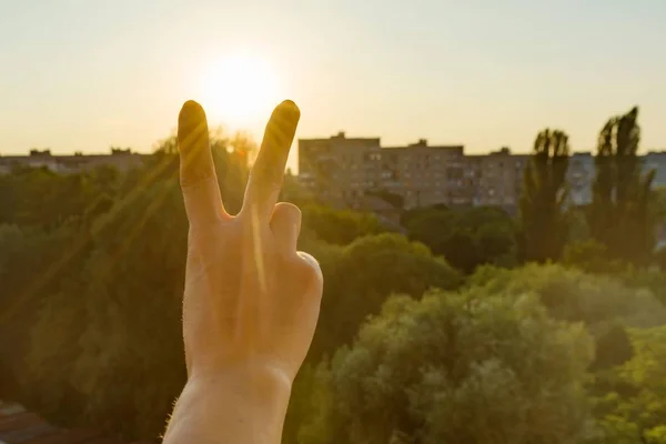 Hand showing two fingers or victory gesture. Background evening sunset, city silhouette