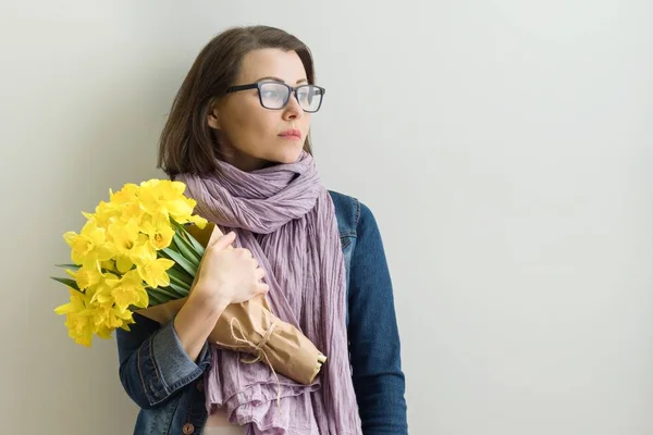 Retrato de uma mulher séria confiante adulta em óculos com buquê de flores amarelas . — Fotografia de Stock