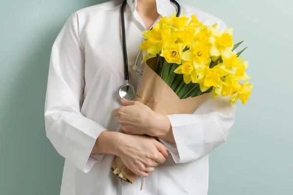 Крупним планом букет жовтих квітів в руках лікаря, пастельний зелений м'ятний фон стіни. Всесвітній день охорони здоров'я, день лікарів — стокове фото
