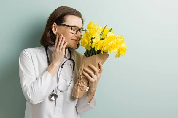 Усміхнена жінка-лікар з букетом квітів, пастельний зелений м'ятний фон стіни. Всесвітній день охорони здоров'я, день лікарів — стокове фото