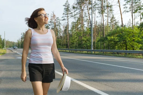 Mature woman walks along the road ahead, looks into the distance, copy space — Stock Photo, Image