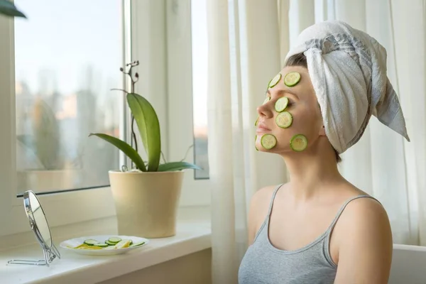Młoda kobieta piękne zbliżenie w domu w pobliżu okna z naturalnych domowe maski ogórka na twarzy, ręcznik na głowę. Skóra, Pielęgnacja, kosmetyki, kosmetologii i dermatologii. — Zdjęcie stockowe