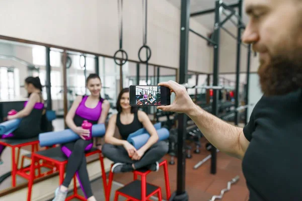 Joven atlética sonriente riendo en el gimnasio, fotografiada en el teléfono móvil. Fitness, deporte, entrenamiento, personas, concepto de estilo de vida saludable . — Foto de Stock