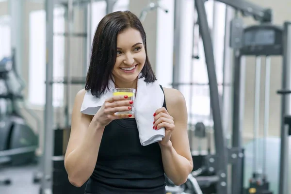 Porträt einer jungen schönen Fitness-Frau in Sportbekleidung mit Handtuch, mit einem Glas Wasser und Zitrone, nach einem Fitnesskurs, der Wasser in der Turnhalle trinkt. gesunde Lebensweise und Ernährung — Stockfoto