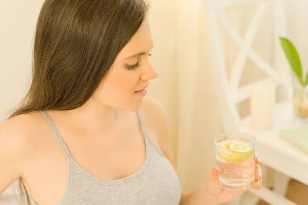 Jeune belle femme boit de l'eau avec du citron assis à la maison au lit, première boisson du matin nourriture saine — Photo