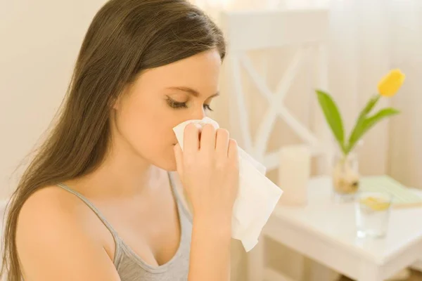 Young woman sitting in bed with handkerchief sneezing. In bedroom yellow spring flower, spring allergy on pollen. — Stock Photo, Image