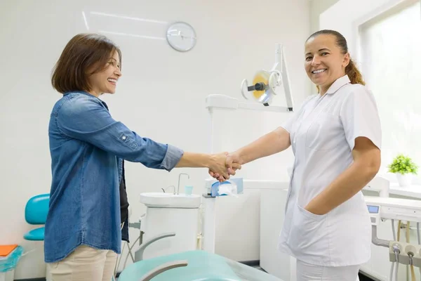Vrouw patiënt schudden van de hand van vrouwelijke tandarts met bezoek in medische kliniek. — Stockfoto