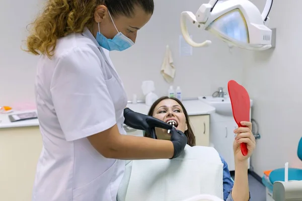 Mature woman patient choosing tooth implant looking at mirror in dental clinic. Medicine, dentistry and healthcare concept. — Stock Photo, Image