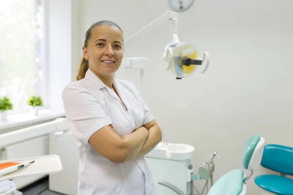 Portret van vrouwelijke tandarts met gekruiste armen, arts glimlachend op tandheelkundige stoel achtergrond. Geneeskunde, tandheelkunde en healthcare concept — Stockfoto