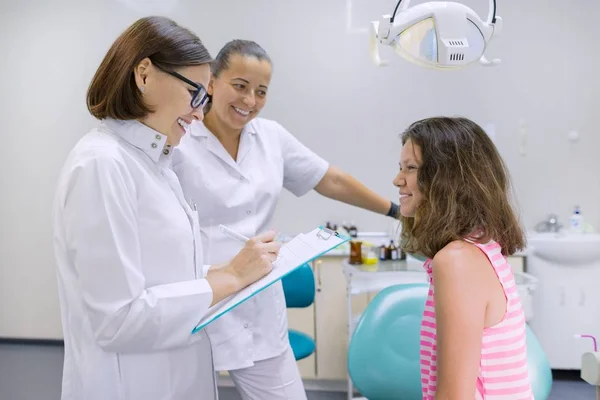 Tonåring flicka pratar med läkare tandläkare sitter i tandläkarens. Medicin, tandvård och sjukvård koncept — Stockfoto