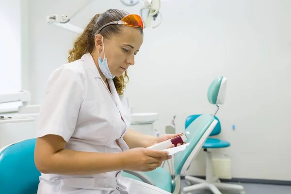 Portret kobieta dentysty, lekarza odczytuje adnotacji instrukcji do leku na tle fotela. — Zdjęcie stockowe