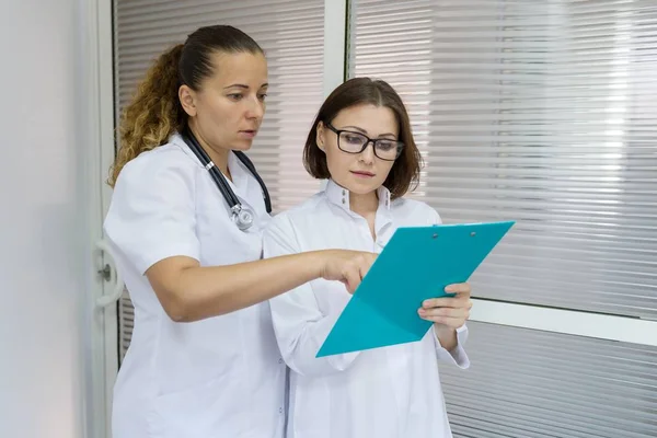 Duas mulheres médico e enfermeira conversando no hospital no fundo da porta — Fotografia de Stock