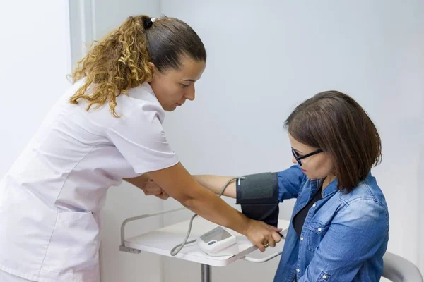 Sjuksköterska att kvinnliga patientens blodtryck i office — Stockfoto