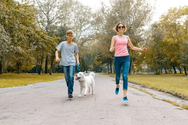 Les adolescents courent avec le chien blanc Husky sur la route dans le parc — Photo