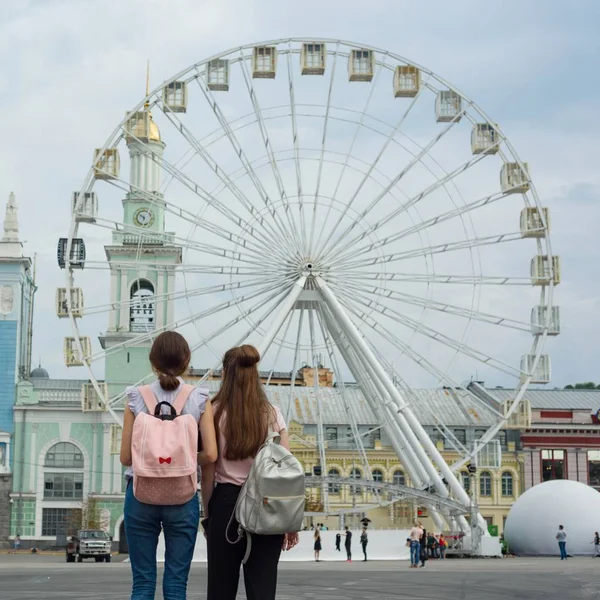 Dvě mladé dívky s batohy při pohledu na ruské kolo, zadní pohled, ve městě — Stock fotografie