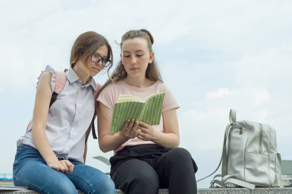 Ritratto all'aperto di due giovani belle ragazze studentesse con zaini, libri. Ragazze che parlano, guardando in un libro — Foto Stock