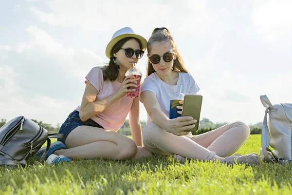 Teens girls in hat and sunglasses on the green lawn in the recreation park enjoying their cocktails, golden hour — Stock Photo, Image