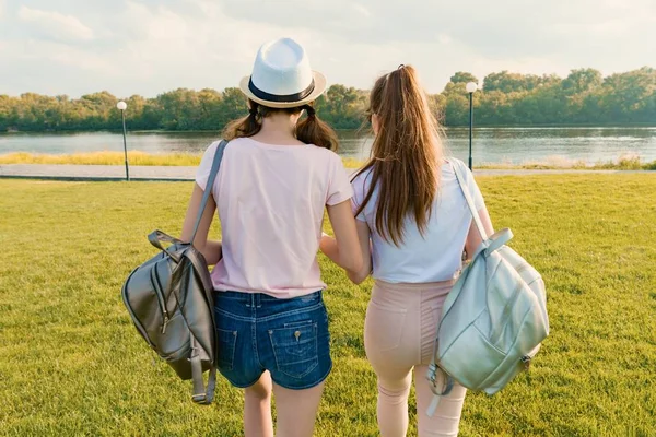 Vista trasera, las amigas están caminando en el parque en la naturaleza. Las niñas caminan por el césped verde, hablan, se divierten — Foto de Stock