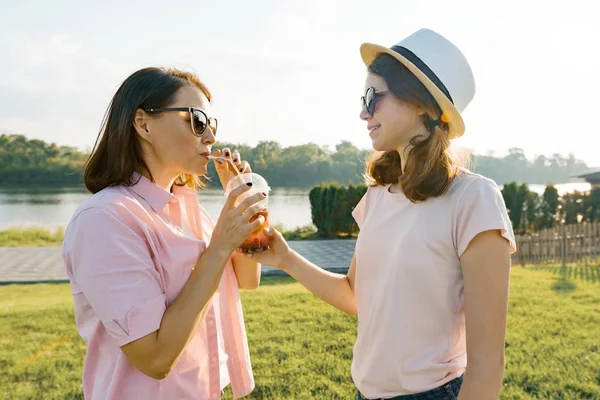 Moeder en dochter chat, lacht moeder en tiener meisje wandeling in de zomer park, dranken drinken, relaxen op het gras, gouden uur — Stockfoto