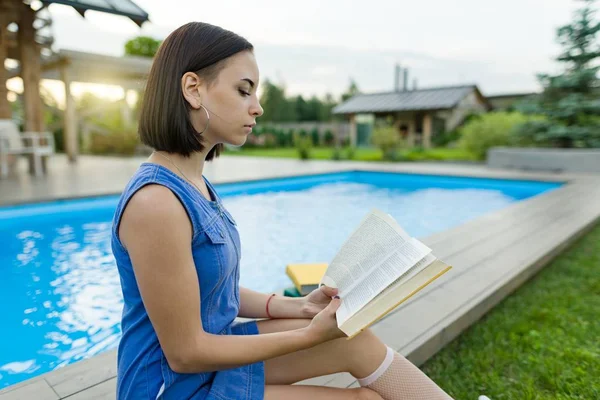 Schattig student meisje het lezen van boeken, achtergrond zwembad, gazon in de buurt van het huis. Onderwijs, zomer, kennis — Stockfoto