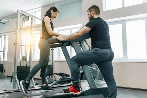 Mujeres atléticas jóvenes en la cinta de correr, instructor personal entrenando y ayudando a la mujer cliente. Fitness, deporte, entrenamiento, concepto de personas . — Foto de Stock