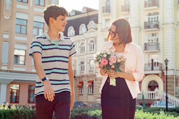 Son är tonåring går med sin mamma utomhus, mamma som innehar bukett blommor gåva från sin son på mors dag. — Stockfoto