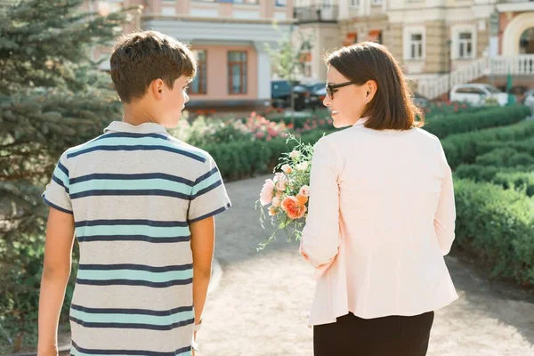 Сын подросток, гуляющий со своей матерью на открытом воздухе, мама держит букет цветов подарок от своего сына на День матери, вид сзади — стоковое фото