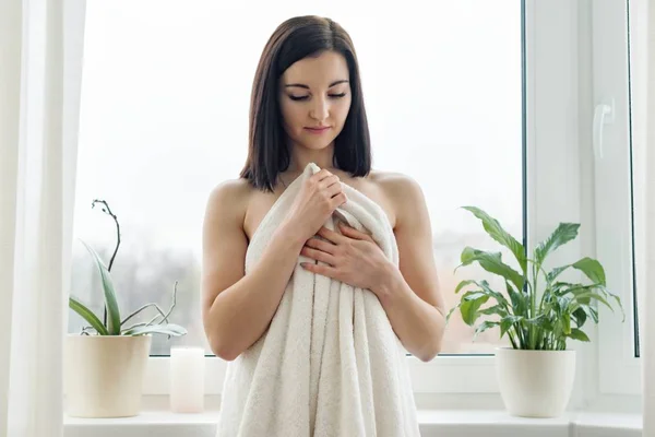 Skjønnhetsportrett av unge brunette kvinner i badehåndkle, spa hjemme. Kvinne som står ved vinduet, ser på kamera, vintersesong, skyet dag – stockfoto