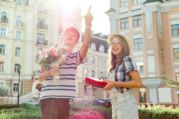 Glada leende tonåringar utomhus, pojke som innehar bukett blommor och flicka med gåva i rutan — Stockfoto