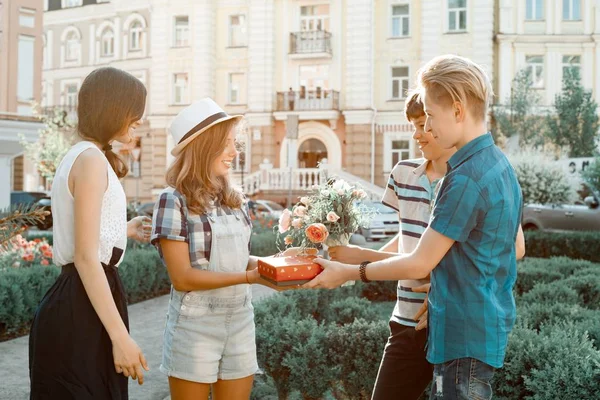 Utomhus porträtt av lycklig grupp av tonåringar vänner gratulera flickan med bukett blommor och gåva i rutan. Kamratskap och folk begrepp — Stockfoto