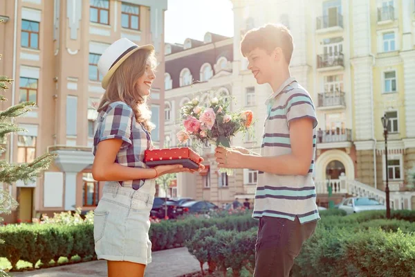 Teen pojke gratulerar flicka med bukett av blommor och gåva, utomhus porträtt par lycklig ungdom — Stockfoto