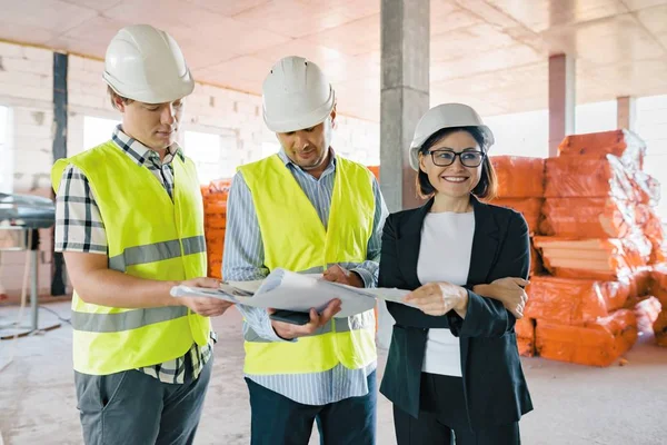 Equipo de ingenieros constructores en el sitio de construcción, lectura de planos. Construcción, desarrollo, trabajo en equipo y concepto de personas — Foto de Stock