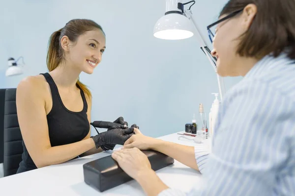 Young lachende vrouw schoonheidsspecialiste in nagel schoonheidssalon doen manicure met professionele gereedschappen, verzorging nagel en hand — Stockfoto