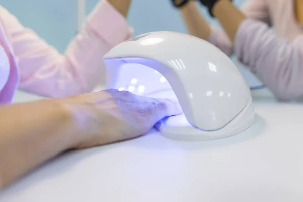 Manicurist using an ultraviolet lamp for fixing gel nail polish. Nail and hand care in beauty salon