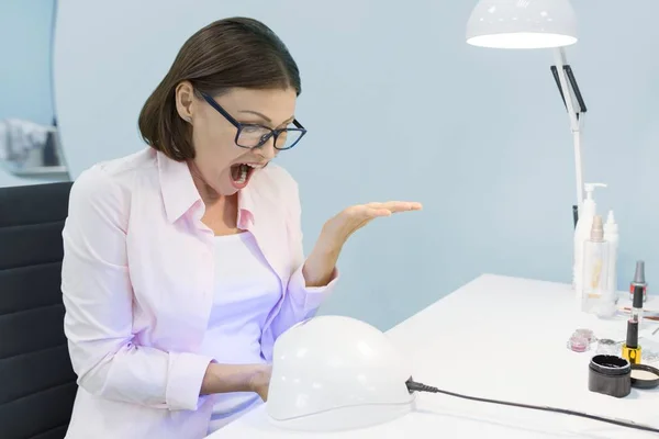 Manicurist using an ultraviolet lamp for fixing gel nail polish. Nail and hand care in beauty salon, woman screams from the pain to her nails under the lamp