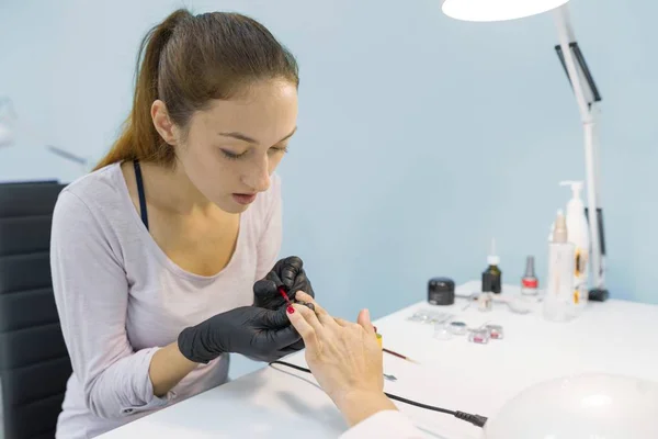 Colored manicure, nail painting. Woman manicurist doing professional manicure, using color gel polish, nail and hand care in beauty salon. — Stock Photo, Image