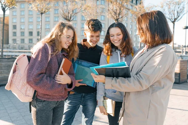 Profesora madura hablando con estudiantes adolescentes fuera de la escuela, hora dorada — Foto de Stock