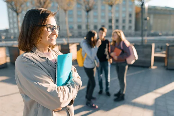 Portret van volwassen glimlachende vrouwelijke leraar in glazen met Klembord, buiten met een groep tieners studenten, Golden Hour — Stockfoto