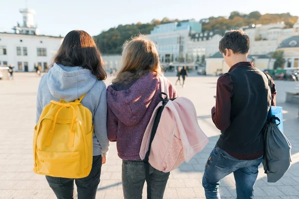 Uitzicht vanaf de achterkant op drie middelbare scholieren. De achtergrond van de stad, gouden uur — Stockfoto