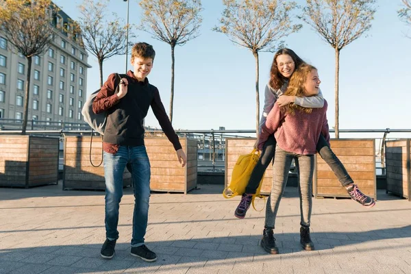Amigos adolescentes estudiantes con bolsas de la escuela, divertirse en el camino de la escuela. Fondo de la ciudad, hora dorada —  Fotos de Stock