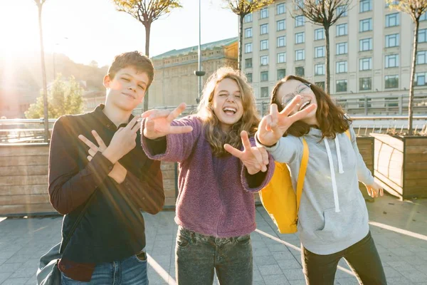 Πορτρέτο των φίλων Έφηβος αγόρι και δύο κορίτσια χαμογελούν, κάνοντας αστεία πρόσωπα, δείχνοντας τη νίκη πινακίδα στο δρόμο. Φόντο πόλης, χρυσή ώρα — Φωτογραφία Αρχείου