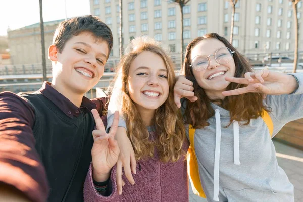 Portret van drie tiener vrienden jongen en twee meisjes glimlachen en het nemen van een selfie buitenshuis. De achtergrond van de stad, gouden uur — Stockfoto