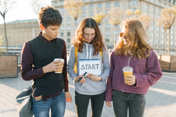 Groep tieners jongen en twee meisjes, met een Kladblok met handgeschreven woord te starten. De achtergrond van de stad, gouden uur — Stockfoto