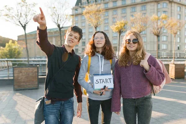 Groep tieners jongen en twee meisjes, met een Kladblok met handgeschreven woord te starten. Tieners kijken uit, stad achtergrond, Golden Hour — Stockfoto