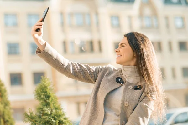 Outdoor portret uśmiechniętej szczęśliwej młodej kobiety ze smartfonem, tło ulicy miasta, jesienny słoneczny dzień — Zdjęcie stockowe